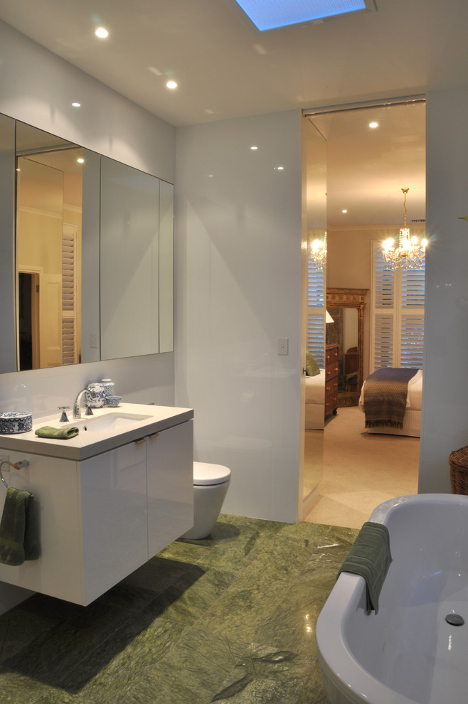 Aménagement d'une salle de bain principale moderne avec un placard à porte plane, des portes de placard blanches, une baignoire indépendante, WC à poser, un carrelage blanc, un mur blanc, un sol en marbre, un lavabo encastré et un sol vert.