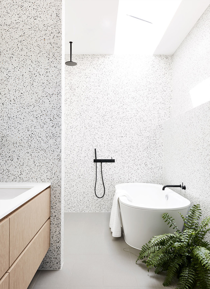Réalisation d'une salle de bain principale design en bois clair avec une baignoire indépendante, un carrelage de pierre, aucune cabine, un placard à porte plane, un carrelage noir et blanc, un mur multicolore, un lavabo encastré et un sol gris.