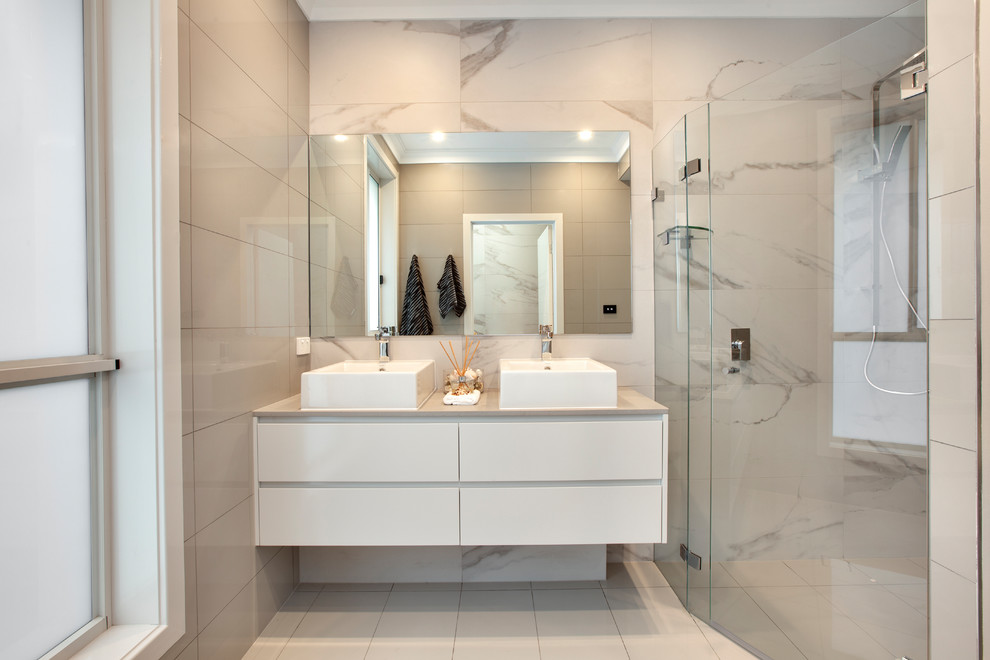 На фото: ванная комната в современном стиле с плоскими фасадами, белыми фасадами, угловым душем, серой плиткой, белой плиткой, разноцветными стенами и настольной раковиной с