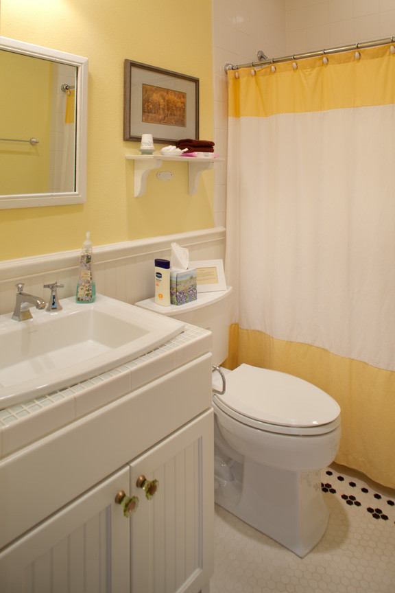 Foto på ett litet lantligt badrum med dusch, med ett nedsänkt handfat, vita skåp, kaklad bänkskiva, ett badkar i en alkov, en dusch/badkar-kombination, en toalettstol med separat cisternkåpa, vit kakel, glaskakel, gula väggar, klinkergolv i keramik och luckor med infälld panel