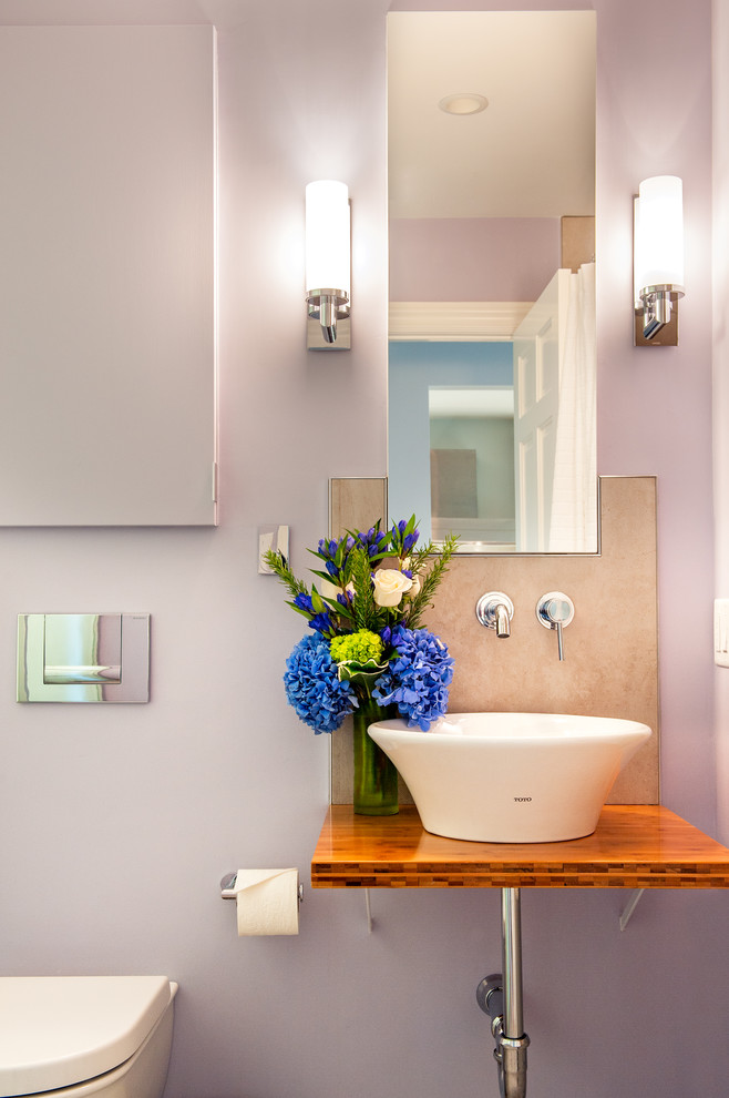 Immagine di una stanza da bagno minimal con lavabo a bacinella, top in legno, WC sospeso, pareti viola e top marrone