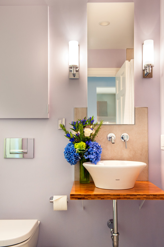 Example of a trendy bathroom design in Boston with a vessel sink, wood countertops, a wall-mount toilet, purple walls and brown countertops