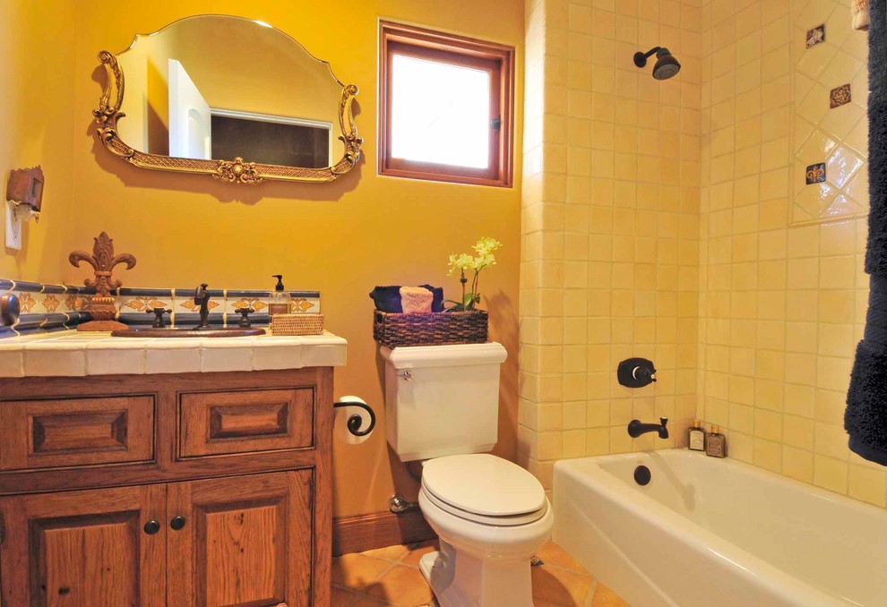 На фото: ванная комната среднего размера в средиземноморском стиле с фасадами с выступающей филенкой, фасадами цвета дерева среднего тона, накладной ванной, душем над ванной, раздельным унитазом, желтой плиткой, керамической плиткой, полом из терракотовой плитки, консольной раковиной и столешницей из плитки