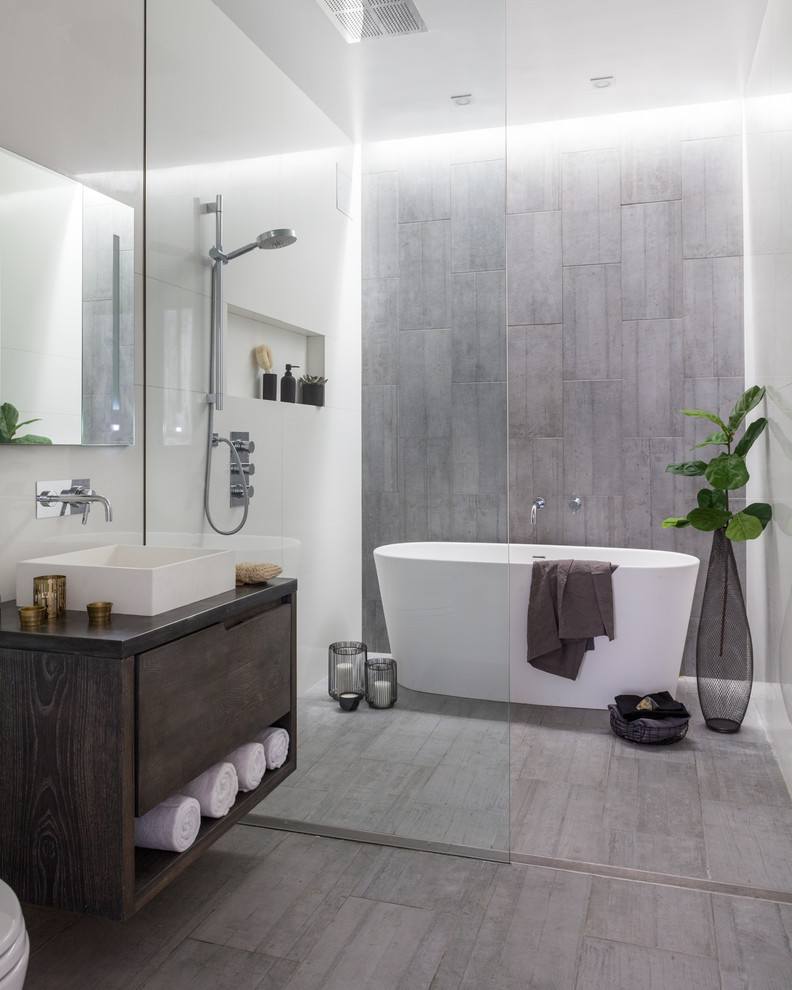 Inredning av ett industriellt litet grå grått en-suite badrum, med ett fristående badkar, våtrum, grå kakel, porslinskakel, vita väggar, klinkergolv i porslin, ett fristående handfat, bänkskiva i zink, grått golv, med dusch som är öppen, släta luckor och skåp i mörkt trä