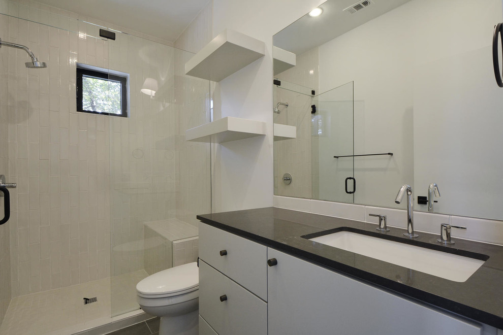 На фото: ванная комната среднего размера в современном стиле с плоскими фасадами, белыми фасадами, душем в нише, раздельным унитазом, белой плиткой, керамогранитной плиткой, белыми стенами, полом из керамогранита, душевой кабиной, врезной раковиной, столешницей из гранита, серым полом, душем с распашными дверями и черной столешницей с
