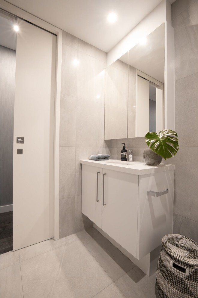 Immagine di una stanza da bagno contemporanea con ante bianche, piastrelle grigie, piastrelle in gres porcellanato, pavimento in gres porcellanato, lavabo sottopiano e top in quarzo composito
