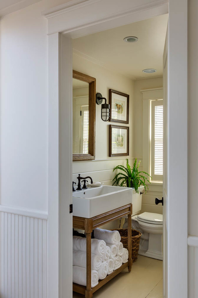 Modelo de cuarto de baño costero de tamaño medio con puertas de armario de madera oscura, sanitario de una pieza, paredes blancas, suelo de madera clara, aseo y ducha y lavabo de seno grande