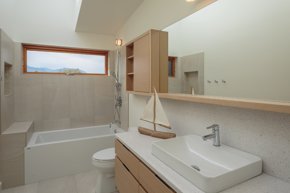 Exemple d'une salle d'eau tendance en bois clair de taille moyenne avec un placard à porte plane, une baignoire en alcôve, un combiné douche/baignoire, un carrelage beige, des carreaux de porcelaine, un mur blanc, un sol en carrelage de porcelaine, une vasque, un plan de toilette en quartz modifié et un sol beige.