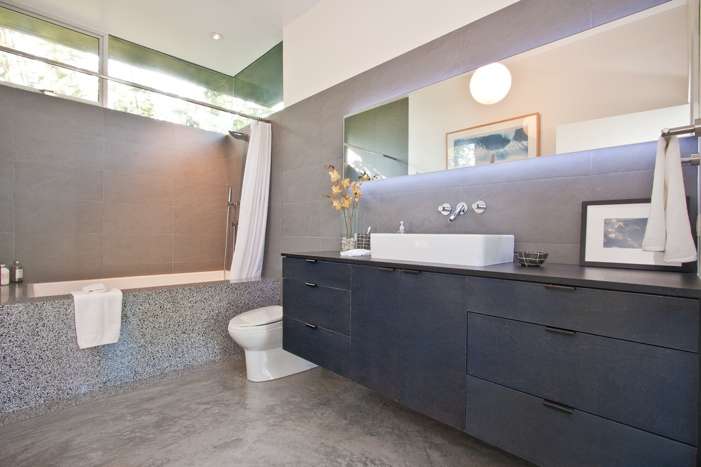 Inspiration för ett mellanstort funkis svart svart en-suite badrum, med ett fristående handfat, dusch med duschdraperi, släta luckor, svarta skåp, ett badkar i en alkov, en dusch/badkar-kombination, en toalettstol med hel cisternkåpa, grå kakel, stenkakel, grå väggar, betonggolv och grått golv