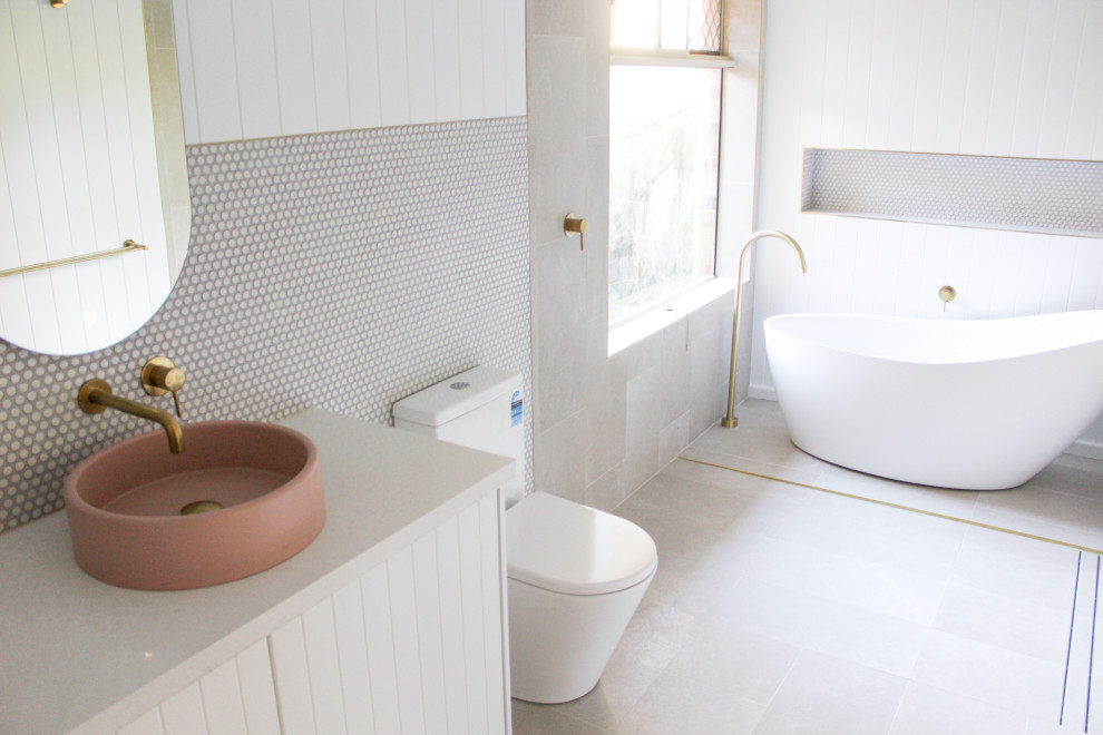 Пример оригинального дизайна: большая главная ванная комната в стиле модернизм с фасадами в стиле шейкер, белыми фасадами, отдельно стоящей ванной, душевой комнатой, унитазом-моноблоком, белой плиткой, галечной плиткой, белыми стенами, полом из керамогранита, настольной раковиной, столешницей из гранита, серым полом, душем с распашными дверями, серой столешницей, нишей, тумбой под две раковины, напольной тумбой и панелями на стенах