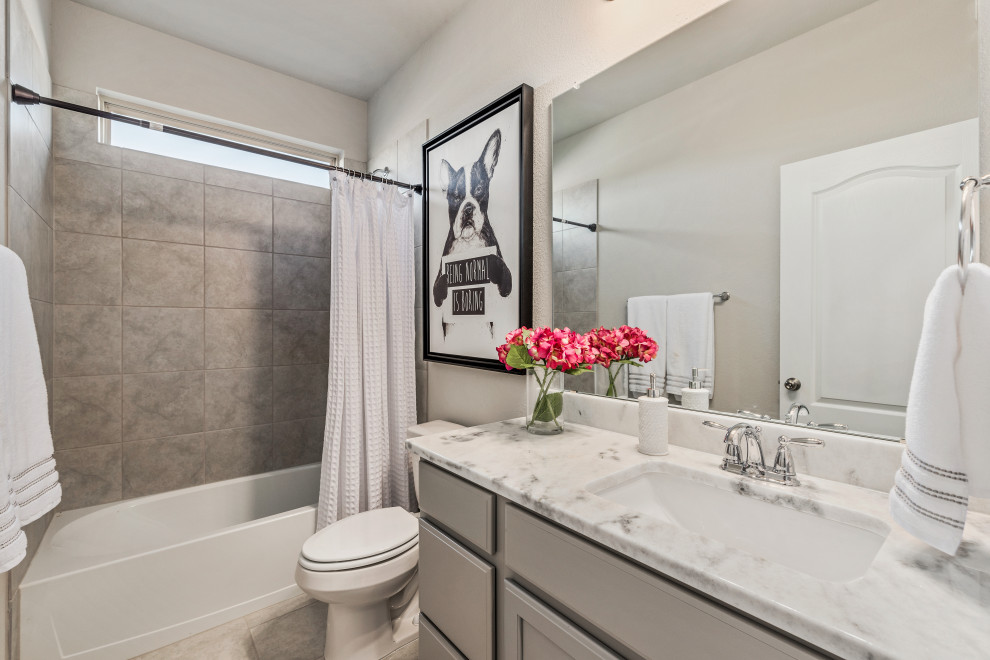 Photo of a large traditional family bathroom in Austin with recessed-panel cabinets, grey cabinets, an alcove bath, a shower/bath combination, a two-piece toilet, grey tiles, ceramic tiles, grey walls, ceramic flooring, a submerged sink, engineered stone worktops, beige floors, a shower curtain, white worktops, a single sink and a built in vanity unit.