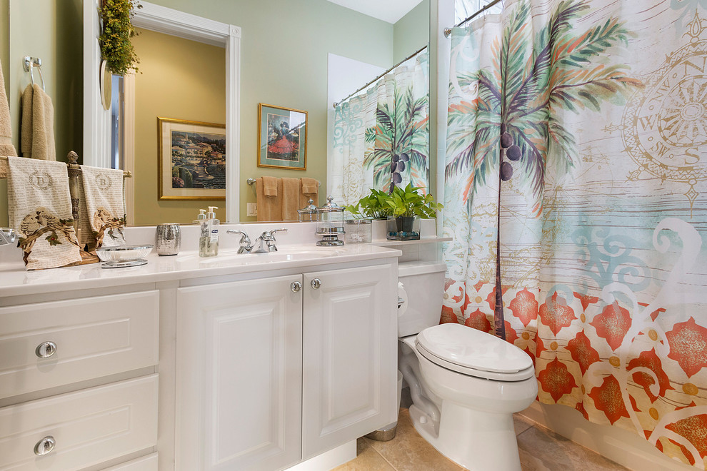Inspiration for a mid-sized tropical 3/4 ceramic tile and beige floor bathroom remodel in Miami with green walls, raised-panel cabinets, white cabinets, a two-piece toilet, an integrated sink, quartz countertops and white countertops