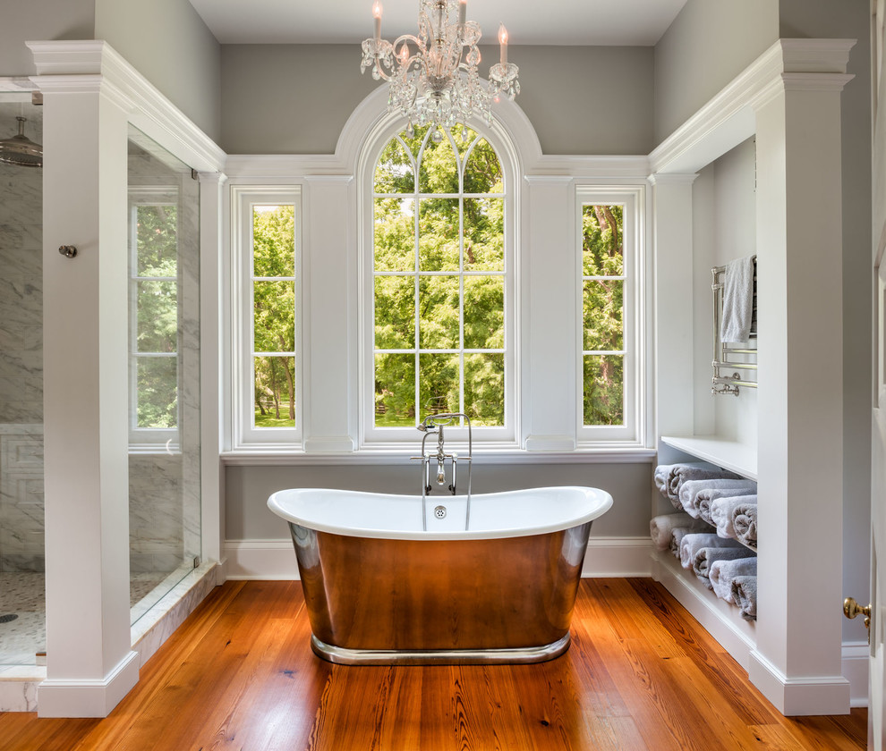 Inredning av ett klassiskt en-suite badrum, med öppna hyllor, vita skåp, ett fristående badkar, en hörndusch, grå väggar och mellanmörkt trägolv