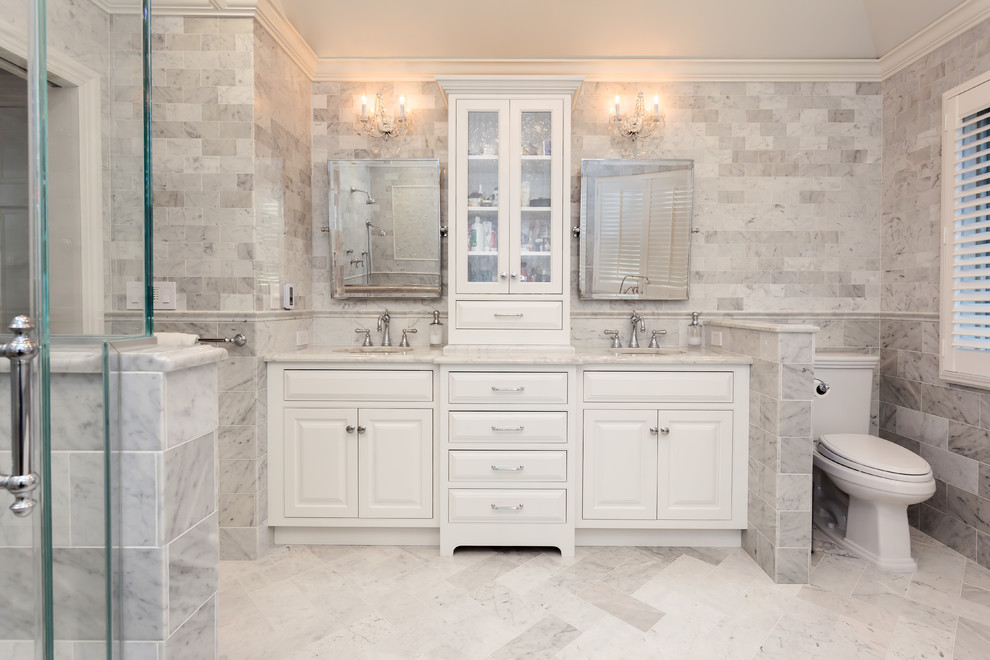 Inredning av ett klassiskt stort en-suite badrum, med ett undermonterad handfat, vita skåp, marmorbänkskiva, ett fristående badkar, en hörndusch, en toalettstol med separat cisternkåpa, vit kakel, stenkakel, grå väggar, marmorgolv och luckor med profilerade fronter
