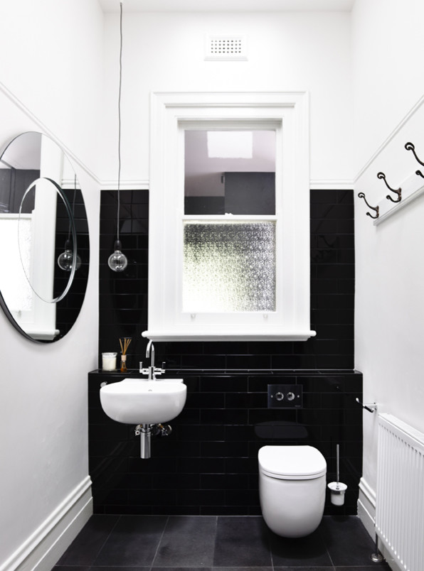 Inredning av ett modernt badrum, med ett väggmonterat handfat, kaklad bänkskiva, en vägghängd toalettstol, svart kakel, keramikplattor och vita väggar