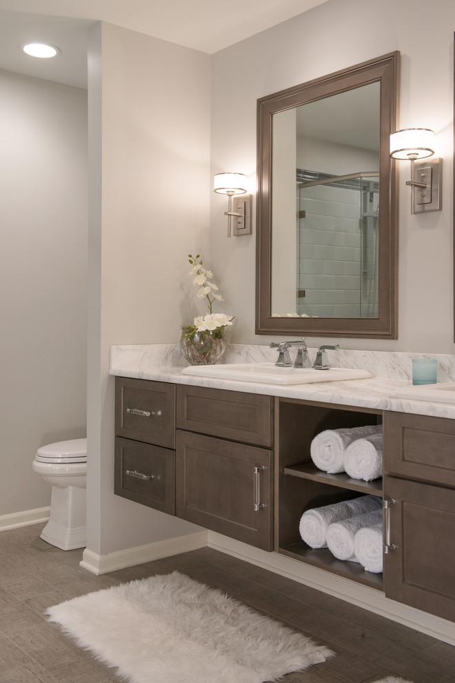Photo of a large classic ensuite bathroom in Kansas City with shaker cabinets, dark wood cabinets, a built-in bath, a corner shower, a two-piece toilet, grey tiles, ceramic tiles, grey walls, porcelain flooring, a built-in sink, granite worktops, grey floors, a hinged door and white worktops.