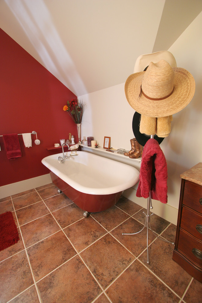 Inredning av ett lantligt stort badrum, med möbel-liknande, skåp i mellenmörkt trä, granitbänkskiva, ett badkar med tassar, en toalettstol med separat cisternkåpa, brun kakel, keramikplattor, röda väggar och klinkergolv i keramik