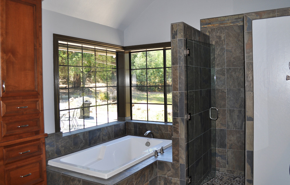 Diseño de cuarto de baño principal con puertas de armario de madera oscura, encimera de mármol, bañera esquinera, ducha esquinera y suelo de pizarra