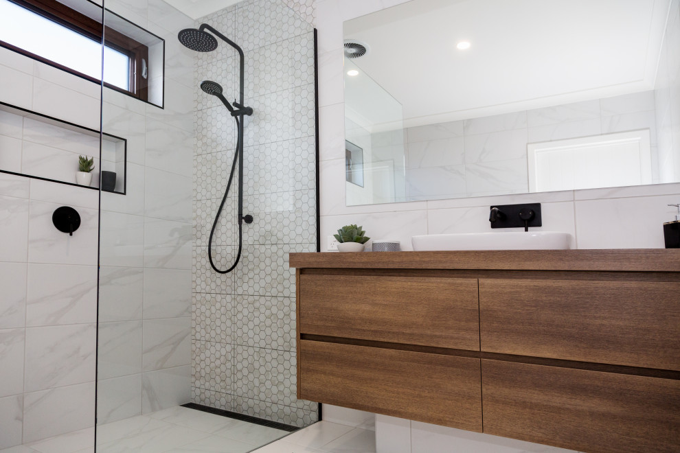 Modelo de cuarto de baño principal actual de tamaño medio con armarios con paneles lisos, puertas de armario marrones, ducha abierta, baldosas y/o azulejos blancos, baldosas y/o azulejos de cerámica, paredes blancas, suelo de baldosas de cerámica, lavabo sobreencimera, encimera de laminado, suelo blanco, ducha abierta y encimeras marrones