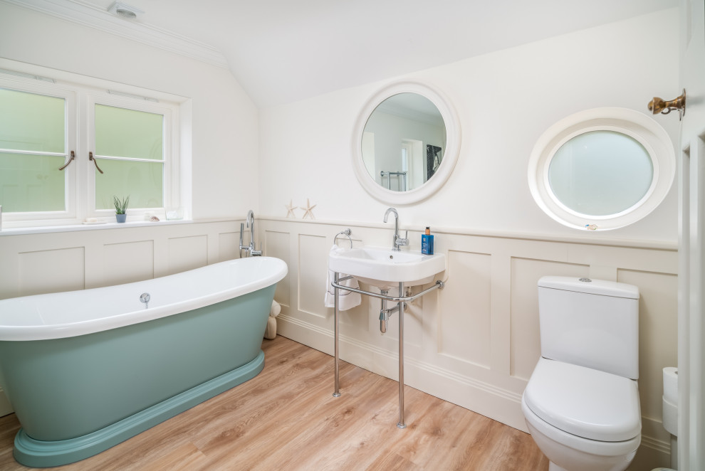 Modelo de cuarto de baño único clásico renovado con sanitario de una pieza, paredes blancas, suelo de madera clara, lavabo tipo consola, suelo beige y boiserie
