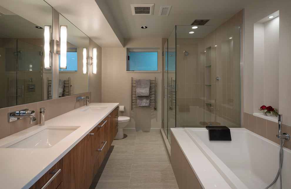 Modelo de cuarto de baño actual con lavabo bajoencimera, armarios con paneles lisos, puertas de armario de madera oscura, ducha esquinera y baldosas y/o azulejos grises