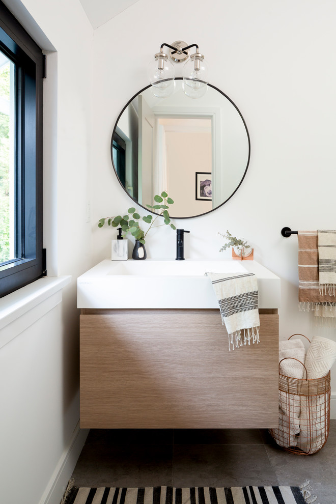 Diseño de cuarto de baño tradicional renovado con armarios con paneles lisos, puertas de armario de madera clara, paredes blancas, lavabo integrado, suelo gris, encimeras blancas y ventanas
