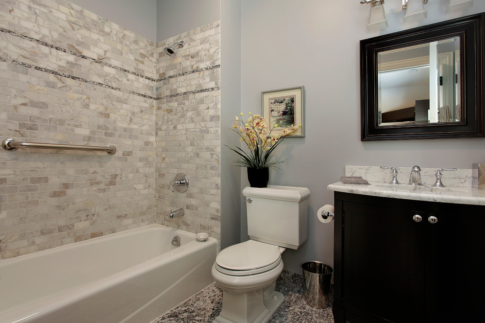 Idée de décoration pour une salle de bain tradition en bois foncé avec un placard avec porte à panneau surélevé, un plan de toilette en marbre, WC séparés, un carrelage gris, un carrelage de pierre et un mur gris.