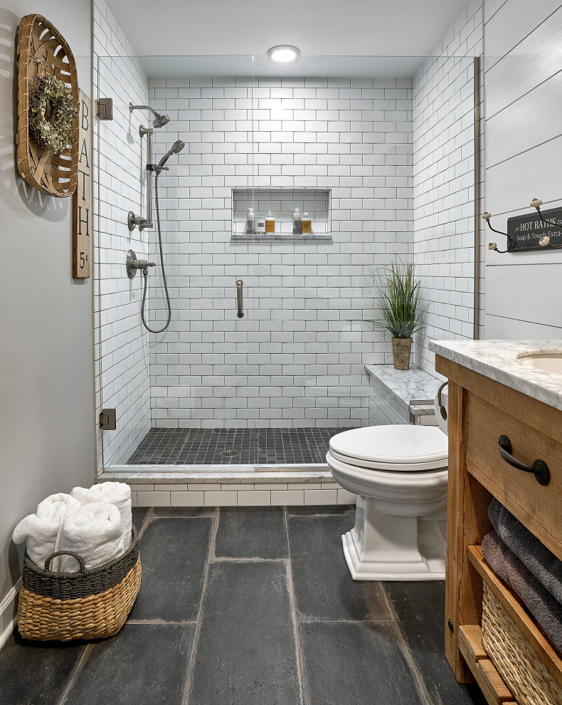 This is an example of a medium sized farmhouse ensuite bathroom in Chicago with distressed cabinets, white tiles, marble worktops, white worktops, a single sink, a freestanding vanity unit, an alcove shower, a two-piece toilet, ceramic tiles, grey walls, porcelain flooring, black floors, a hinged door, a shower bench, tongue and groove walls, a submerged sink and flat-panel cabinets.