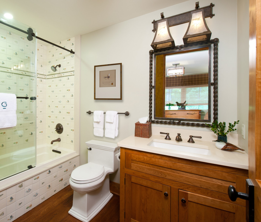 Example of a small classic kids' medium tone wood floor bathroom design with shaker cabinets, medium tone wood cabinets, a one-piece toilet, green walls, an undermount sink, quartz countertops and beige countertops