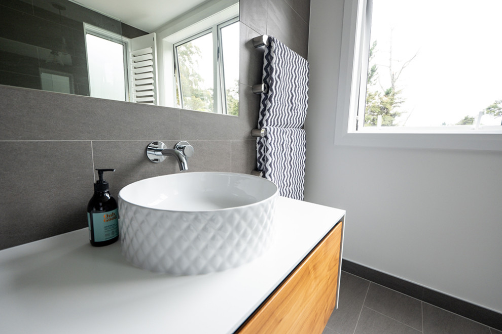 Cette image montre une salle de bain design avec un carrelage gris, des carreaux de céramique, un mur gris, un sol en carrelage de céramique, une vasque, un plan de toilette en quartz modifié, un sol gris, un plan de toilette blanc, meuble double vasque et meuble-lavabo sur pied.