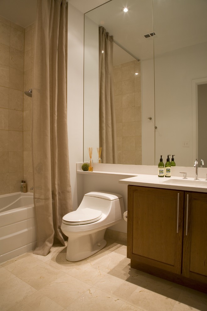 Cette image montre une salle de bain design en bois brun avec un lavabo intégré, un placard à porte shaker, un combiné douche/baignoire, WC à poser, un carrelage beige et un plan de toilette blanc.