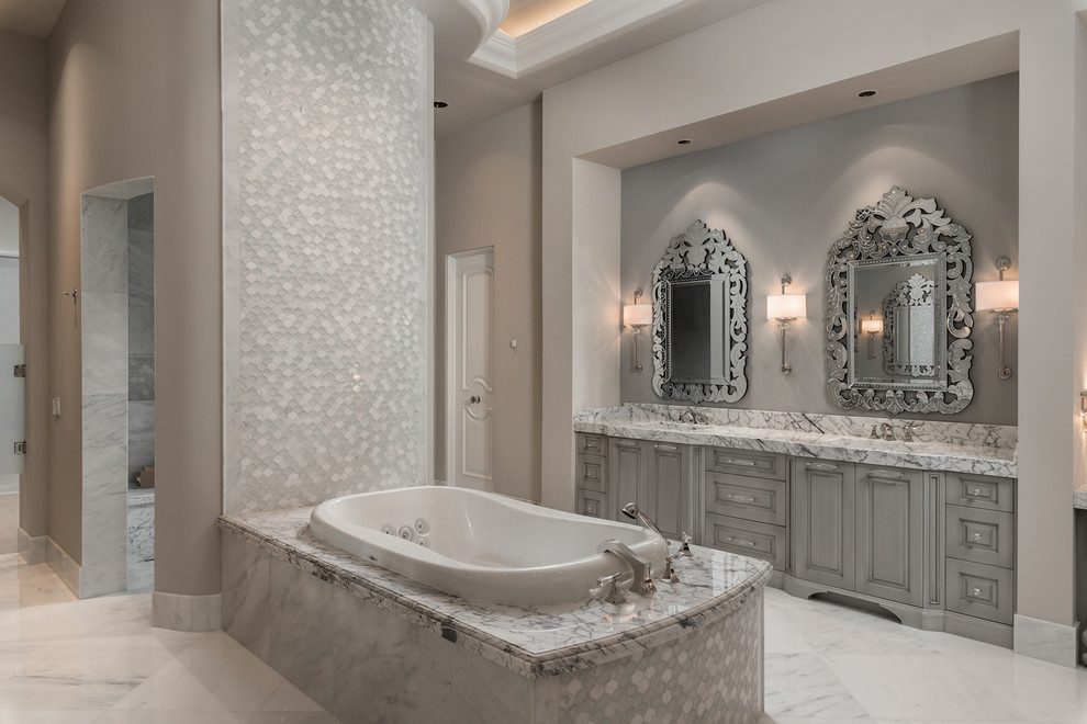 На фото: огромная главная ванная комната в средиземноморском стиле с фасадами с выступающей филенкой, серыми фасадами, накладной ванной, открытым душем, унитазом-моноблоком, разноцветной плиткой, мраморной плиткой, бежевыми стенами, мраморным полом, монолитной раковиной, мраморной столешницей, разноцветным полом, открытым душем, разноцветной столешницей, нишей, тумбой под две раковины, встроенной тумбой, кессонным потолком и панелями на части стены с