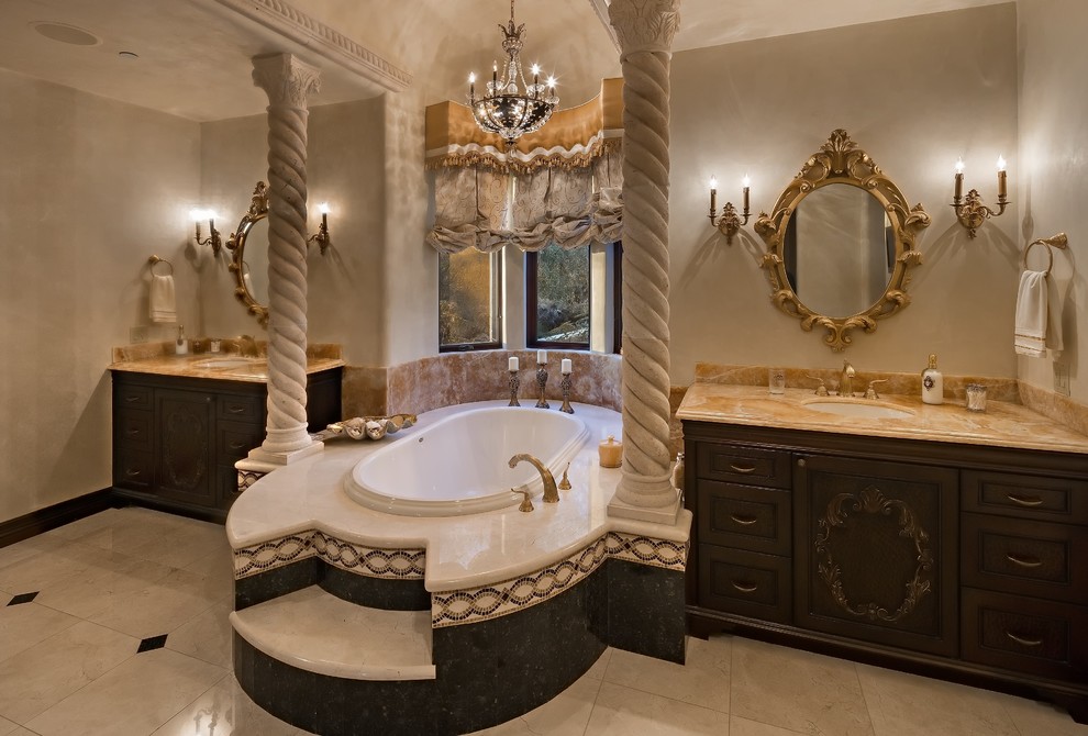 This is an example of a large mediterranean ensuite bathroom in Phoenix with freestanding cabinets, dark wood cabinets, a built-in bath, a double shower, a one-piece toilet, beige tiles, stone tiles, beige walls, travertine flooring, a submerged sink and quartz worktops.