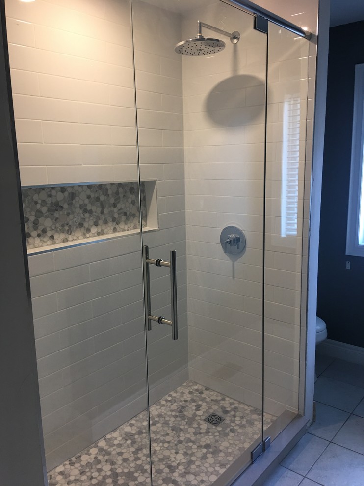 Cette photo montre une petite salle de bain moderne pour enfant avec une douche double, un carrelage blanc, des carreaux de porcelaine, un sol en galet, un lavabo encastré et une cabine de douche à porte battante.