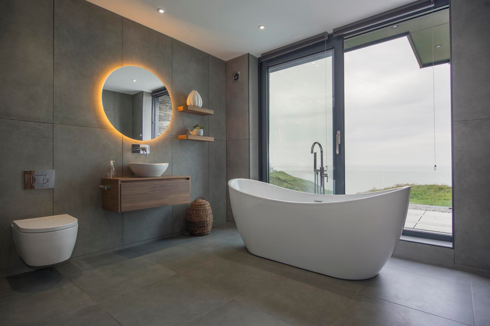 Design ideas for a contemporary ensuite bathroom in Other with flat-panel cabinets, medium wood cabinets, a freestanding bath, a wall mounted toilet, grey tiles, a vessel sink, wooden worktops, grey floors and brown worktops.