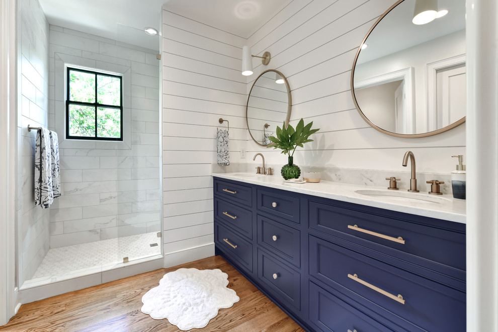 Klassisk inredning av ett vit vitt badrum, med luckor med infälld panel, blå skåp, en dusch i en alkov, vit kakel, vita väggar, mellanmörkt trägolv, ett undermonterad handfat, brunt golv och med dusch som är öppen