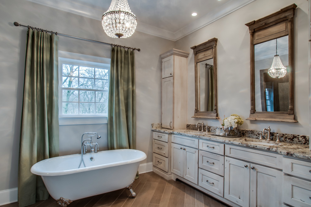 Ejemplo de cuarto de baño principal clásico con armarios con paneles empotrados, puertas de armario con efecto envejecido, encimera de granito y bañera exenta