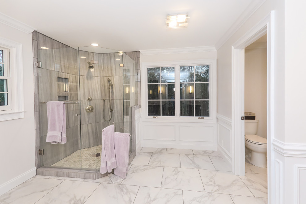 Large classic ensuite bathroom in Atlanta with freestanding cabinets, grey cabinets, a corner shower, a two-piece toilet, grey tiles, porcelain tiles, white walls, porcelain flooring, a submerged sink, engineered stone worktops, white floors, a hinged door, grey worktops, double sinks, a built in vanity unit, a shower bench and wainscoting.