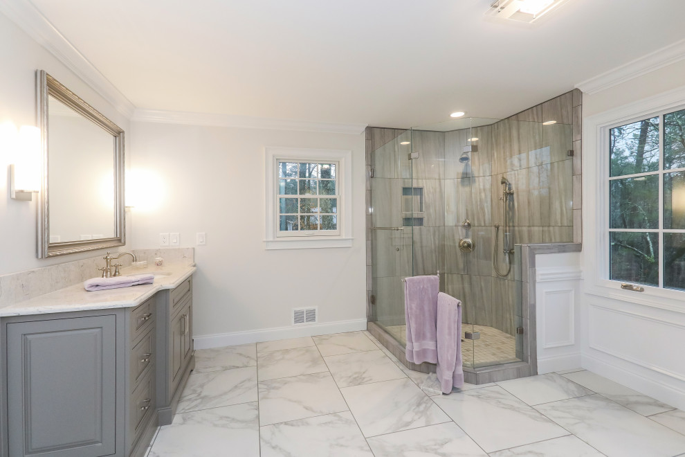 Стильный дизайн: большая главная ванная комната в стиле неоклассика (современная классика) с серыми фасадами, угловым душем, раздельным унитазом, серой плиткой, керамогранитной плиткой, белыми стенами, полом из керамогранита, врезной раковиной, столешницей из искусственного кварца, белым полом, душем с распашными дверями, серой столешницей, нишей, тумбой под две раковины, встроенной тумбой, панелями на стенах и фасадами с выступающей филенкой - последний тренд