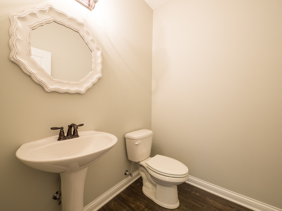 Esempio di un bagno di servizio stile americano di medie dimensioni con WC a due pezzi, pareti beige, parquet scuro e lavabo a colonna