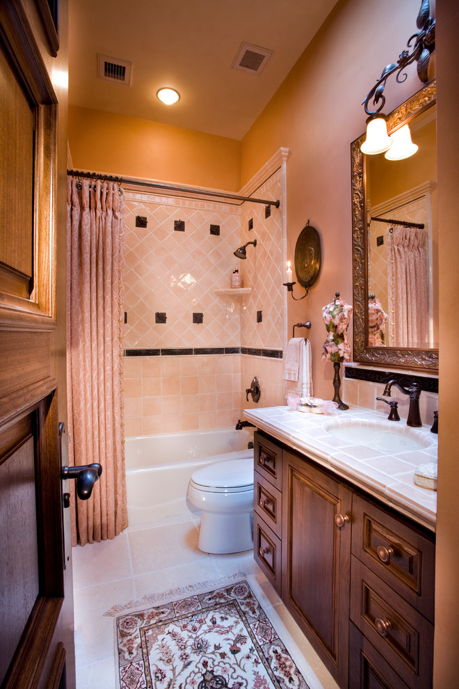 Пример оригинального дизайна: ванная комната среднего размера в классическом стиле с фасадами с выступающей филенкой, темными деревянными фасадами, ванной в нише, душем над ванной, раздельным унитазом, розовой плиткой, керамической плиткой, розовыми стенами, полом из известняка, врезной раковиной и столешницей из плитки