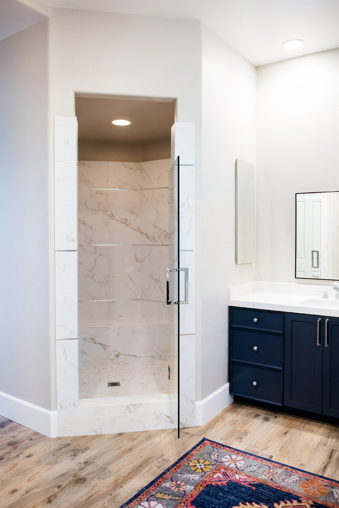 Large classic ensuite bathroom in San Diego with recessed-panel cabinets, blue cabinets, a built-in bath, a corner shower, a two-piece toilet, grey tiles, white tiles, marble tiles, beige walls, porcelain flooring, a submerged sink, engineered stone worktops, brown floors, a hinged door and white worktops.