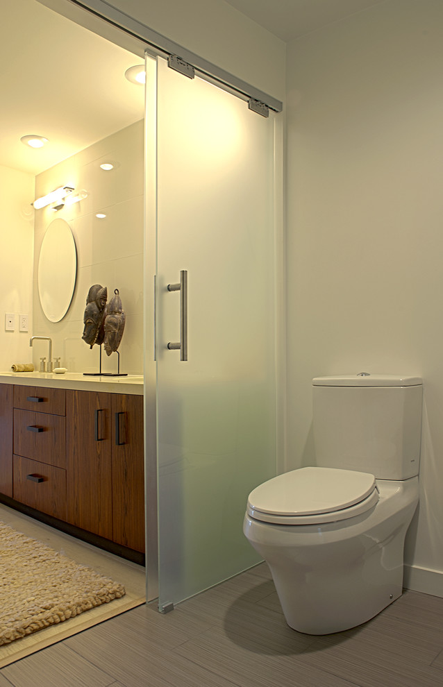Diseño de cuarto de baño actual con armarios con paneles lisos, puertas de armario de madera oscura y sanitario de dos piezas