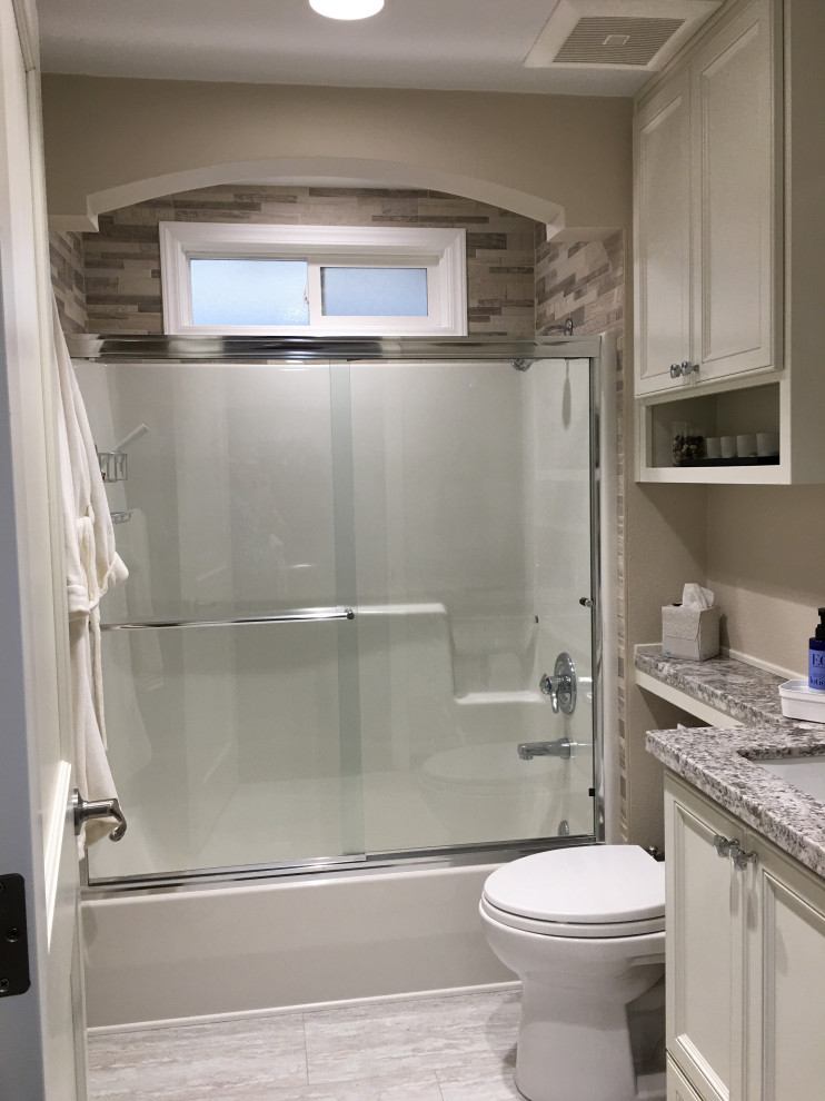 Bathroom - mid-sized traditional beige tile and stone tile linoleum floor, gray floor and single-sink bathroom idea in Portland with raised-panel cabinets, white cabinets, a two-piece toilet, beige walls, an undermount sink, granite countertops, gray countertops, a niche and a built-in vanity