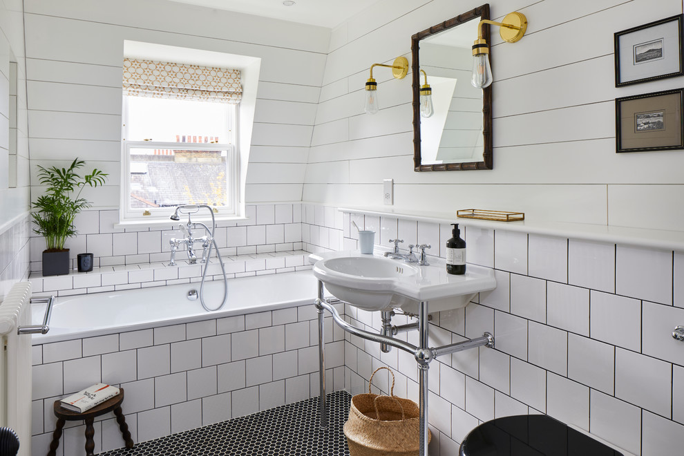 Modelo de cuarto de baño tradicional con bañera encastrada, baldosas y/o azulejos blancos, paredes blancas, suelo con mosaicos de baldosas, lavabo tipo consola, suelo negro y espejo con luz