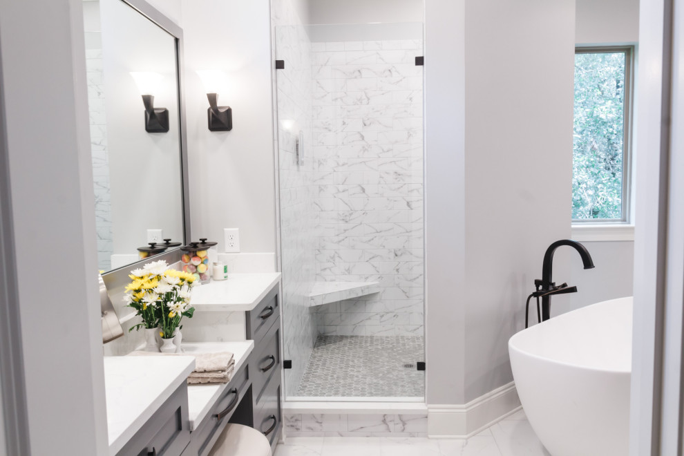 Cette image montre une grande salle de bain principale minimaliste avec un placard à porte shaker, des portes de placard grises, une baignoire indépendante, une douche d'angle, WC à poser, un carrelage gris, des carreaux de céramique, un mur gris, un sol en carrelage de céramique, un lavabo encastré, un plan de toilette en quartz modifié, un sol blanc, une cabine de douche à porte battante, un plan de toilette blanc, un banc de douche, meuble simple vasque et meuble-lavabo encastré.