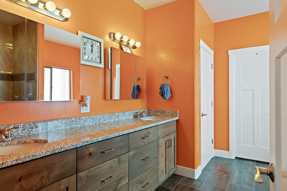 This is an example of a medium sized country ensuite bathroom in Other with shaker cabinets, medium wood cabinets, a built-in bath, a walk-in shower, a one-piece toilet, grey tiles, ceramic tiles, orange walls, ceramic flooring, a submerged sink, granite worktops, black floors and grey worktops.