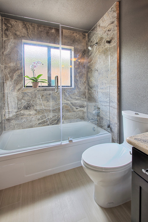 Ispirazione per una stanza da bagno con doccia minimal di medie dimensioni con ante in legno bruno, vasca ad alcova, vasca/doccia, WC monopezzo, piastrelle beige, pareti grigie e parquet chiaro