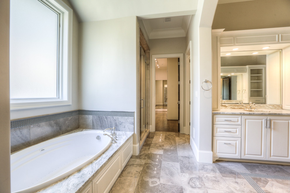 Aménagement d'une grande salle de bain principale classique avec un placard avec porte à panneau surélevé, des portes de placard blanches, une baignoire en alcôve, un mur beige, un lavabo encastré, un plan de toilette en marbre et un sol beige.