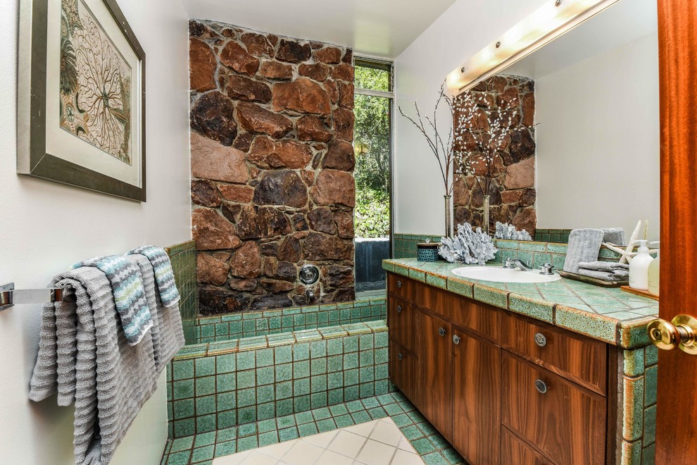 Photo of a large retro ensuite bathroom in San Francisco with flat-panel cabinets, dark wood cabinets, an alcove bath, brown tiles, green tiles, stone tiles, white walls, ceramic flooring, a built-in sink, tiled worktops, green floors and green worktops.